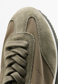 Sneaker in suede verde e tessuto con tomaia texturizzata, punta arrotondata e lacci a contrasto con cucitura lungo i bordi.