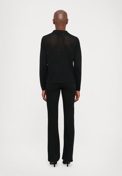 Black sweater with a knitted texture and collar, featuring a sheer striped back design. Paired with black fitted pants and high heels.