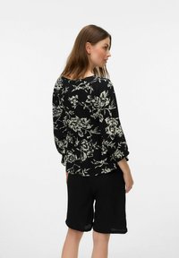 Blouse noire à fleurs avec des manches amples, présentant des imprimés botaniques blancs. Associée à un short noir, cela crée une tenue décontractée.