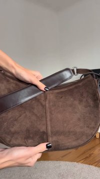 Rjava torbica za ramena iz semiša z gladkim usnjenim trakom, okroglo obliko in vidnimi šivi.