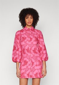 Vestido floral rosa com frente abotoada, apresentando mangas bufantes e um padrão texturizado. Feito de um tecido leve com detalhes intrincados.