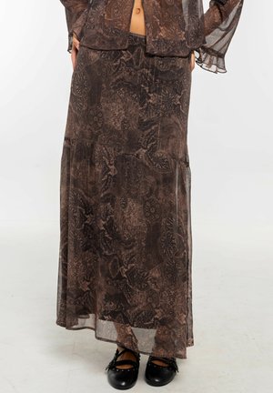 Falda larga transparente de patrón marrón combinada con un top de manga larga a juego, llevados con zapatos planos negros de tiras.