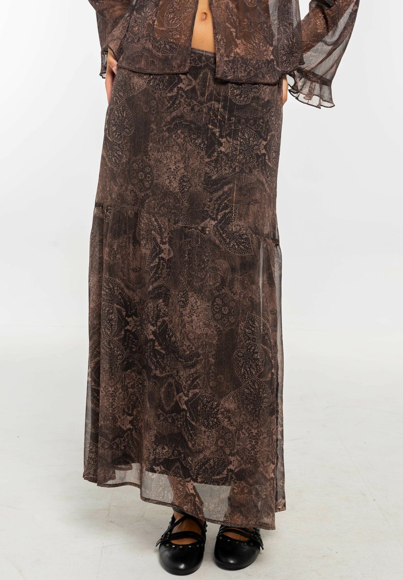 Falda larga transparente de patrón marrón combinada con un top de manga larga a juego, llevados con zapatos planos negros de tiras.