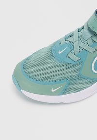 Baskets légères de sport dans des teintes de teal et d'aqua, présentant un dessus en mesh, un col rembourré, des accents blancs et une semelle blanche flexible.