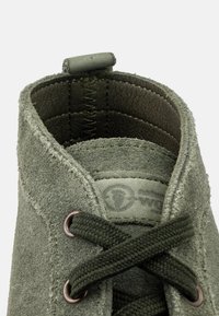 Stivale alla caviglia verde in suede con una texture morbida, dotato di punta rotonda, occhielli in metallo e una foderatura interna testurizzata.