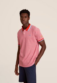 Rood en wit gestreept poloshirt met een kraag, voorzien van blauwe accenten bij de kraag en mouwen, gedragen met marineblauwe shorts.