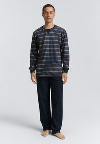 Haut à rayures à manches longues en bleu marine avec des rayures claires, associé à un pantalon sombre à coupe décontractée. Fabriqué en tissu doux ; présente un col rond.