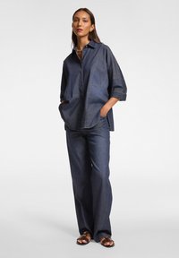 Camicia di denim e pantaloni a gamba larga in blu scuro. La camicia presenta un colletto, bottoni e tasche laterali. I pantaloni hanno una vestibilità comoda e una leggera elasticità.