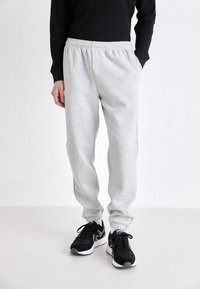 Lichtgrijze sweatpants met een elastische tailleband en geboeide enkels, gecombineerd met zwarte sportschoenen. Zachte textuur, casual pasvorm.