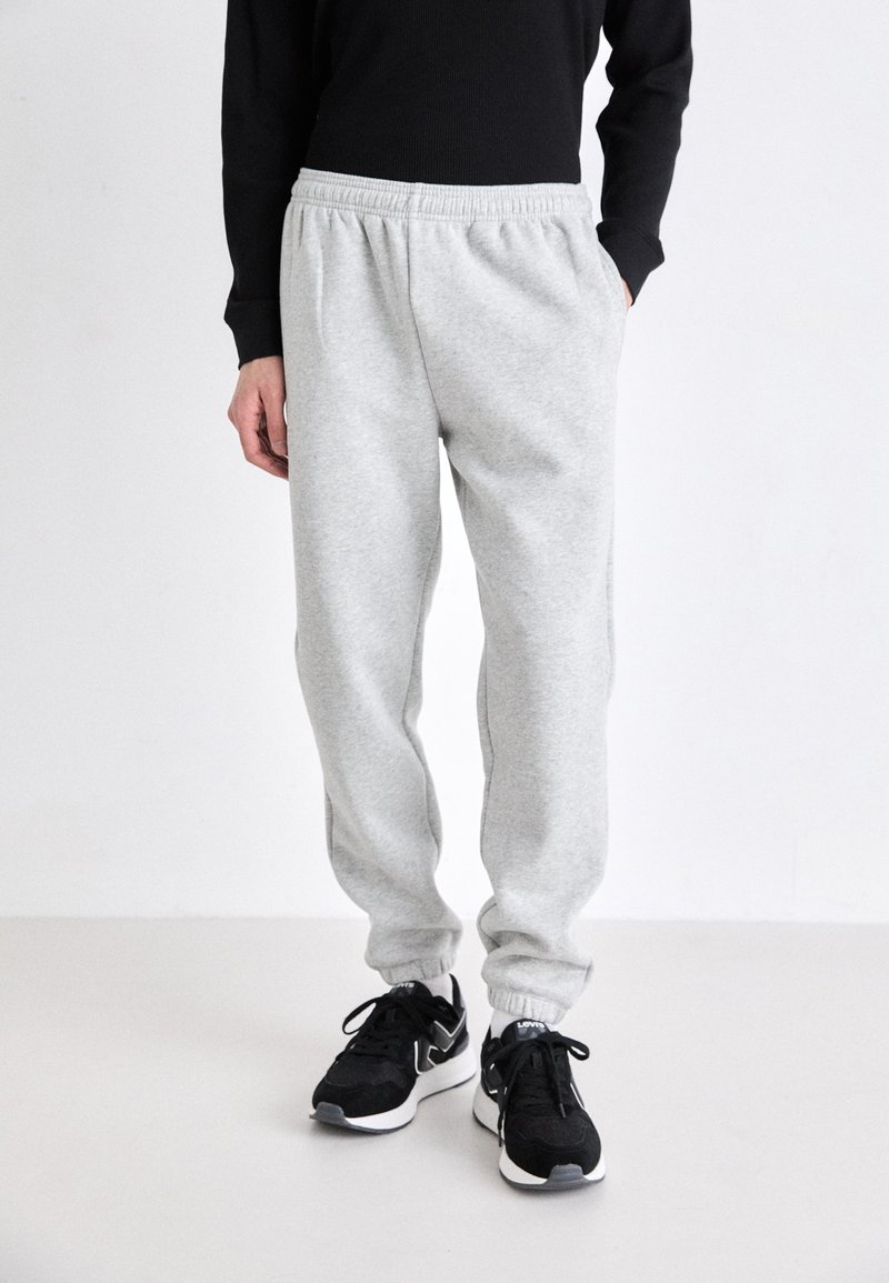 Lichtgrijze sweatpants met een elastische tailleband en geboeide enkels, gecombineerd met zwarte sportschoenen. Zachte textuur, casual pasvorm.