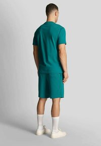 T-shirt di cotone turchese abbinata a pantaloncini coordinati. L'outfit presenta una vestibilità comoda ed è completato da calzini bianchi e sneakers.