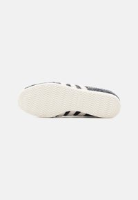 Black and white athletic shoe sole with zigzag tread pattern, featuring three black stripes and a textured surface.