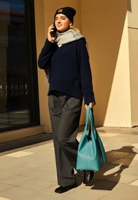 Granatowy sweter wełniany, szare dopasowane spodnie, czarne buty i turkusowa torebka. Lekki szalik dopełnia stylizację. Modelka rozmawia przez telefon.