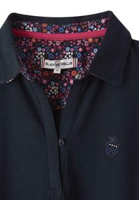 Polo marine en tissu texturé, avec un col intérieur à motifs floraux, un petit logo sur la poitrine et une patte de boutonnage à trois boutons.