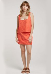 Ensemble deux pièces corail comprenant un haut sans manches et une jupe assortie, tous deux ornés de broderies florales et de bords festonnés.