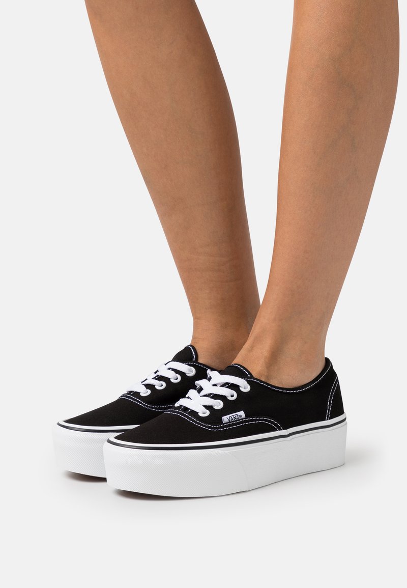 Black canvas sneakers with white rubber soles, featuring white laces and contrasting stitching on the upper. Classic low-profile design.