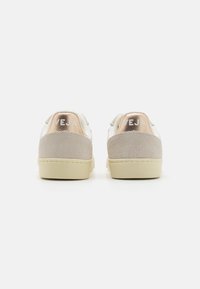 Sneakers in pelle bianca con inserti in suede beige e dettagli metallici in rosa oro sul tallone. Presentano il logo "VEJA" impresso. Design a punta rotonda.