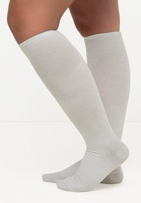 Calcetines hasta la rodilla en material acanalado de color gris claro, con una textura suave y punta reforzada, diseñados para la comodidad y el soporte.