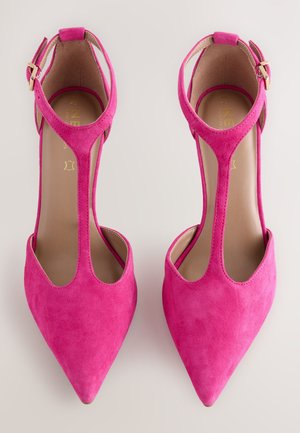 Roosad seemisnahast kõrge kontsaga kingad, millel on terav ninatükk, lõigatud küljed ja reguleeritav pahkluu rihm kuldse pandlaga. Lamedad, tekstureeritud tallad.