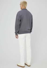 Un sweat-shirt gris avec une coupe décontractée, des poignets et un col côtelés, associé à un jean blanc et des baskets crème. Fond uni, sans motifs.