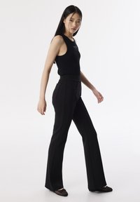 Černý žebrovaný top bez rukávů v kombinaci s černými slim-fit kalhotami s vysokým pasem, které mají boční kapsy a rovné nohavice. Elegantní, minimalistický design.