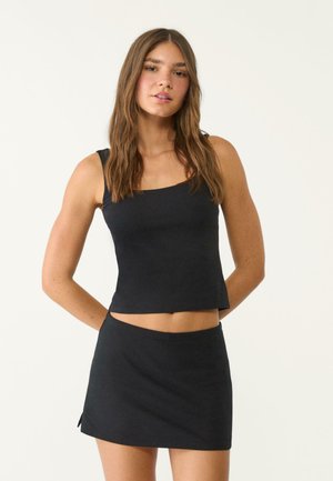 Set composto da top corto nero e mini gonna, realizzato in tessuto elasticizzato, con scollatura quadrata e spacchi laterali nella gonna per una maggiore libertà di movimento.