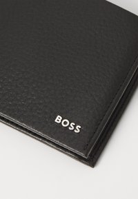 Carteira preta em couro com superfície texturizada, bordas costuradas e um logótipo prateado "BOSS" no canto inferior.