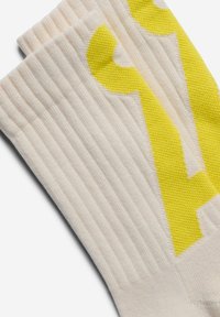 Cremefarbene, gerippte Socken mit einem auffälligen gelben Grafikmuster, einer glatten Textur und kontrastierenden Farben für visuelles Interesse.