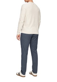 Cremfarbener strukturierter Sweatshirt mit gerippter Bündchen, kombiniert mit marineblauen gemusterten Hosen und weißen Sneakers mit dunklen Akzenten.
