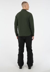 Donkergroene overhemd met lange mouwen en een opstaande kraag, gecombineerd met zwarte, loszittende broek. Gladde textuur, lichtgewicht stof, minimalistisch ontwerp.