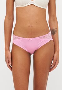 Panty in nylon rosa con bordino in pizzo, caratterizzata da un delicato fiocco al centro e una texture liscia in tutto il capo.