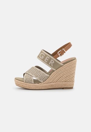 Sandales à talons compensés beiges en matériau raffia tressé, avec un design à bandes croisées et une bride de cheville ajustable marron. Accent logo sur les bandes.