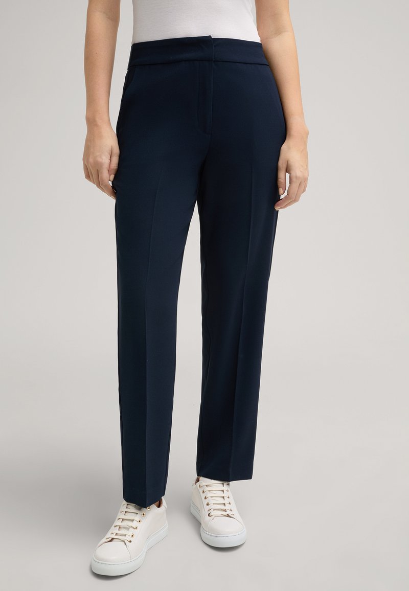 Marineblaue maßgeschneiderte Hose aus einem glatten, leichten Stoff, mit geradem Schnitt und frontalen Taschen, kombiniert mit weißen Sneakers.