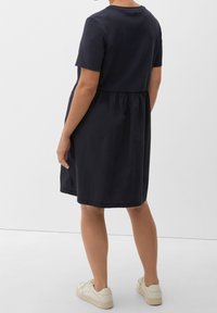 Robe en coton bleu marine avec manches courtes, taille froncée et ourlet à hauteur du genou, associée à des baskets de couleur claire.