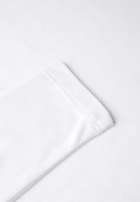 Eck einer weißen Baumwoll-T-Shirt mit einem gefalteten Ärmel und genähtem Rand, der eine glatte Textur und klare Linien aufweist.