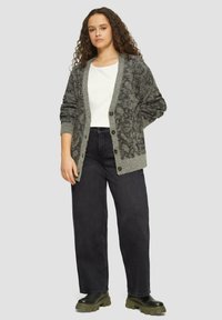 Grauer Cardigan mit strukturiertem Design, Knopfverschluss vorne und kontrastierenden Bündchen. Kombiniert mit schwarzen,weit geschnittenen Jeans und dunklen Stiefeln.