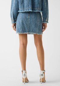 Minigonna in tweed blu con orli sfrangiati, abbinata a una giacca coordinata. Sandali argentati con tacco alto completano l'outfit. Accessori minimal.