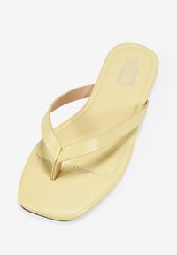 Chancla amarilla con un acabado brillante y elegante, que presenta una tiras en forma de V para el dedo del pie y una suela cuadrada. Parte superior texturizada con un ligero detalle de costura.