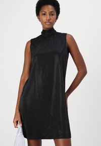 Svart ärmlös klänning med hög hals, som har ett strukturerat tyg med en subtil lyster och en avslappnad silhuett. Faller mjukt.