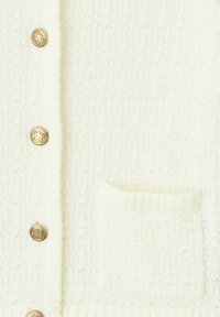 Cardigan blanc en tricot avec un motif texturé, des boutons dorés et une petite poche carrée à l'avant. Tissu doux et respirant.