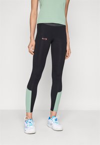 Black athletic leggings with mint green panels, featuring a pink logo on the hip and a textured waistband. Worn with a green top and white shoes.