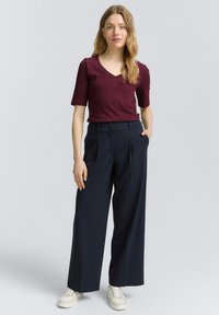 Bordeaux korte mouw V-hals top gecombineerd met marineblauwe wijde broek met hoge taille en zijzakken, gedragen met witte sneakers.