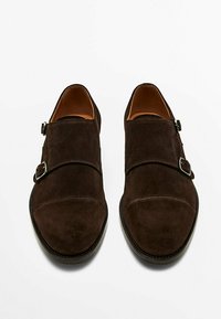 Ruske suede čevlji s okroglim nosom, opremljeni z dvema prilagodljivima zaponkama in šivano obrobo ob robovih. Ravna podplat.