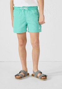 Turquoise zwembroek met elastische tailleband en koord, gecombineerd met grijze sandalen met een kurken zool en een kruisriemdesign.