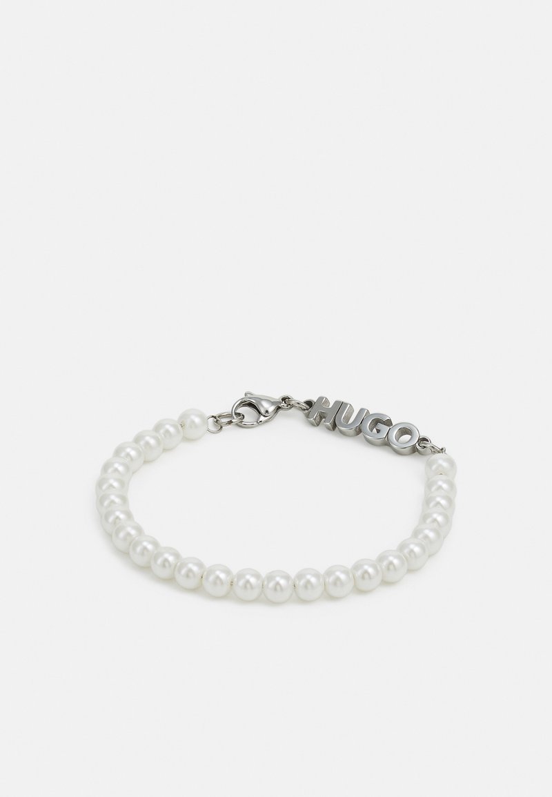 Bracelet avec des perles blanches rondes et un fermoir en argent avec le mot "HUGO" en lettres majuscules.