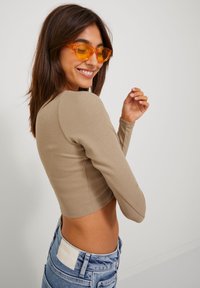 Khaki hosszú ujjú bordázott crop top, magas derekú kék farmerral párosítva. A modellen átlátszó narancssárga keretes napszemüveg van. Sima textúra, testhezálló kialakítás.