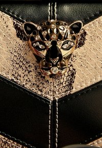 Decorațiune cu cap de leopard incrustat cu bijuterii aurii și negre pe o suprafață din piele texturată albă și bej, cu cusături albe.