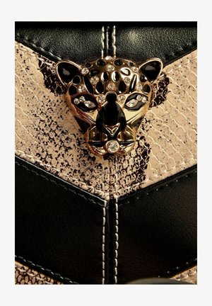 Zlatno i crno ukrašena leopardova glava na crnoj i bež teksturiranoj kožnoj površini s bijelim šavovima.