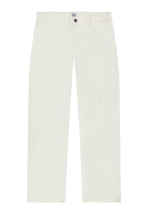 Kobieta ubrana w całkowicie biały strój z koszulą na krótki rękaw z guzikami, spodniami z wysokim stanem, czarnym wzorzystym szalikiem i czarnymi trampkami, stojąca na szarym tle.