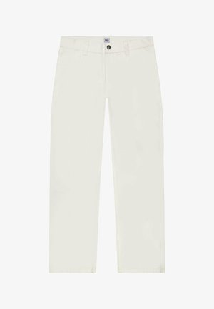 Kobieta ubrana w całkowicie biały strój z koszulą na krótki rękaw z guzikami, spodniami z wysokim stanem, czarnym wzorzystym szalikiem i czarnymi trampkami, stojąca na szarym tle.